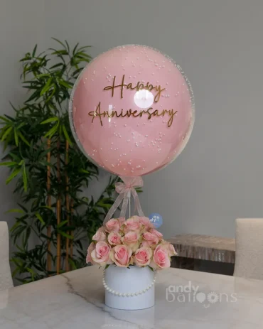 Fresh pink roses in a white box topped with a pink bubble balloon featuring a gold Happy Anniversary message.