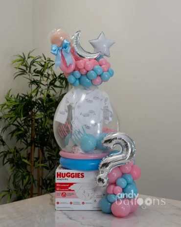Gender reveal balloon arrangement with a diaper box and a stuffed balloon containing a baby onesie. Decorated with pink and blue balloons.