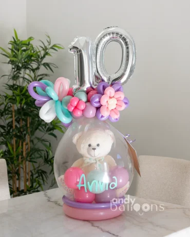 Personalized stuffed balloon gift featuring a plush teddy bear inside, topped with a silver number ten and colorful floral balloon accents.
