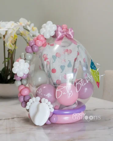 Personalized baby arrival balloon with "Welcome Baby" message, pink and purple balloon accents, and a baby onesie inside.